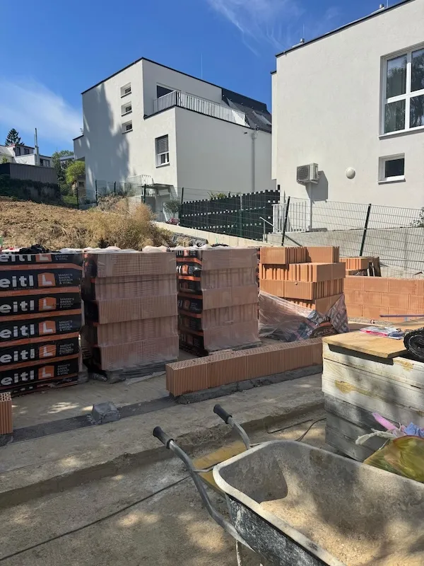 baustelle mit ziegelsteinen und schubkarre zwischen modernen wohnhäusern