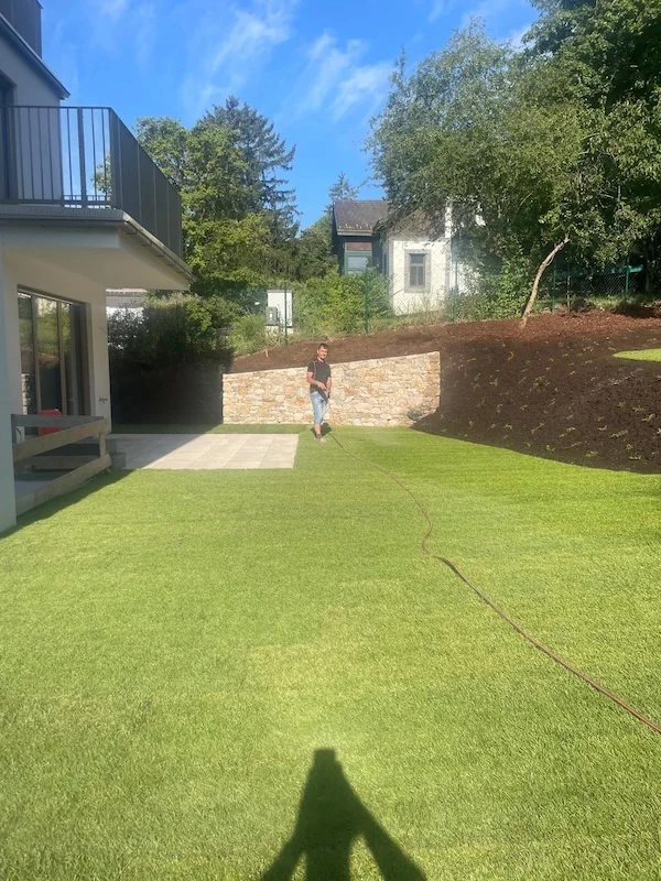 garten eines modernen hauses mit frisch verlegtem rasen und steinmauer